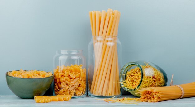 Side view of different types of macaroni as bucatini spaghetti vermicelli and others on wooden surface and blue background