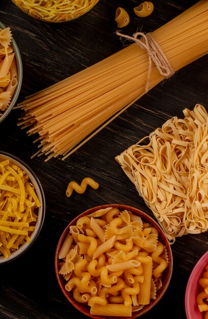 Side view of different types of macaroni as spaghetti vermicelli tagliatelle and others on wooden table