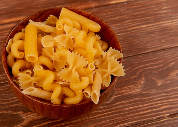 Side view of different types of macaroni in bowl on wooden table with copy space