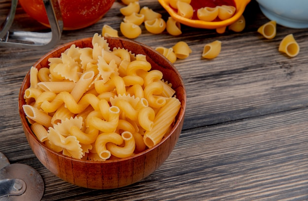 Side view of different types of macaroni in wooden bowl on wooden table