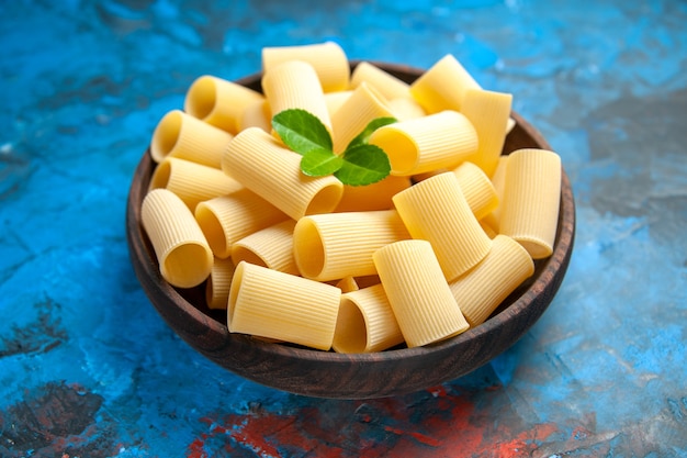 Side view of dinner preparation with pasta noodles with green in a brown pot on blue background