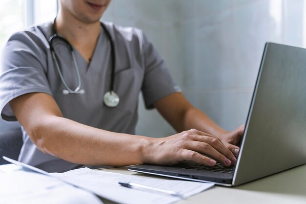 Side view of doctor with stethoscope working on laptop