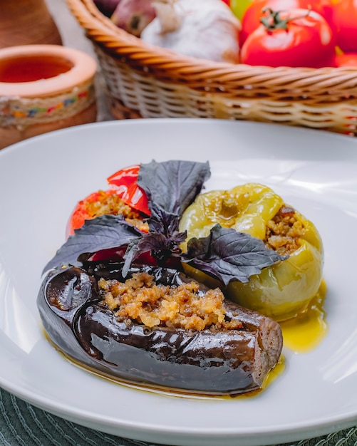Free photo side view dolma stuffed eggplant tomato bell pepper with ground meat and basil on a plate