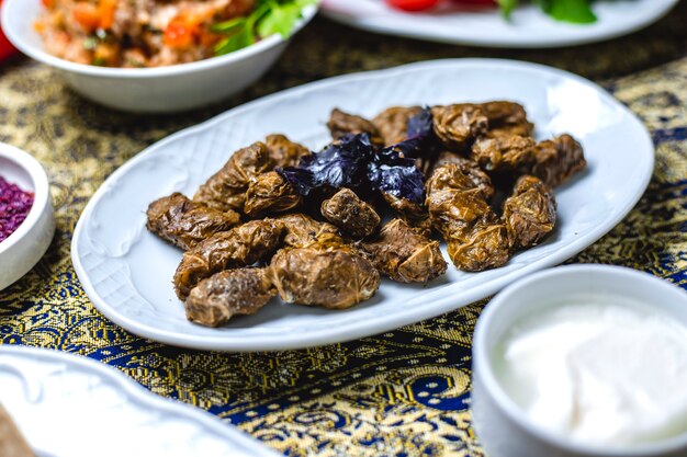 Foto gratuita vista laterale dolma farcito foglie di vite con cipolla macinata sale pepe basilico e yogurt sul tavolo