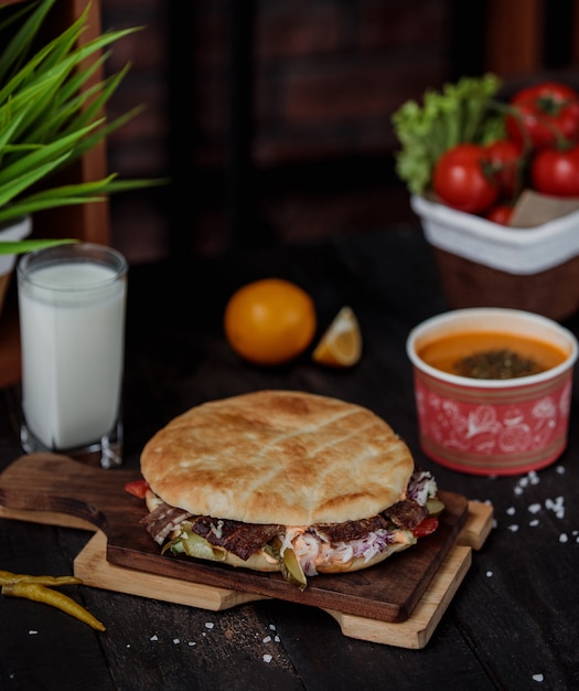 Side view of doner kebab in pita bread on a wooden board served with lintel soup and ayran drink on the table