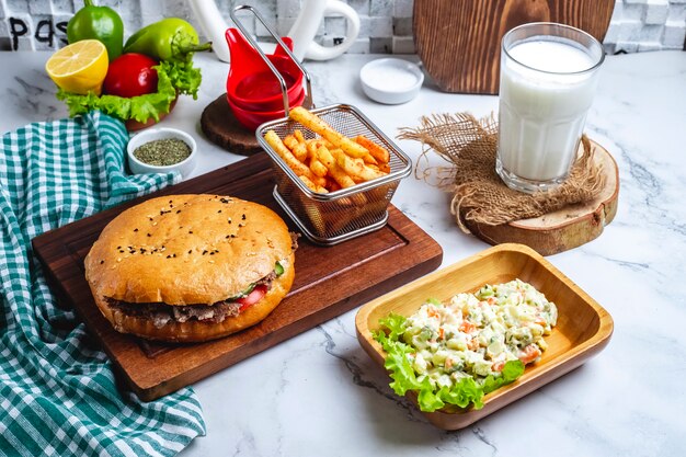 Вид сбоку донер-кебаб с мясом в лаваше на деревянной доске с овощным салатом, картофелем фри и айранским напитком