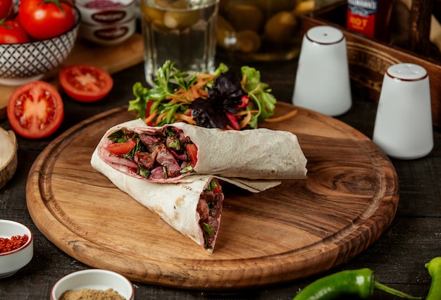 Side view of doner kebab wrapped in lavash with fresh salad on wooden board