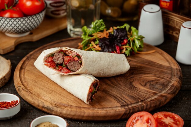 Side view of doner kebab wrapped in lavash with fresh salad on wooden board
