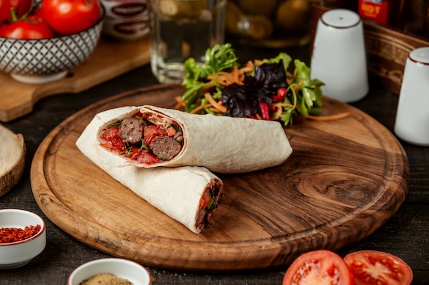 Side view of doner kebab wrapped in lavash with fresh salad on wooden board