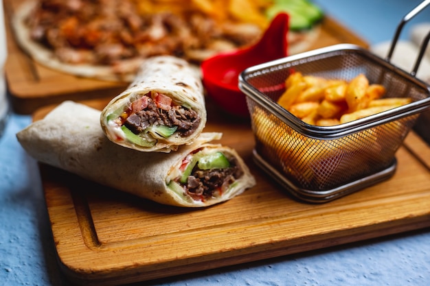 Side view doner with meat cucumber tomato sauce and french fries on a board