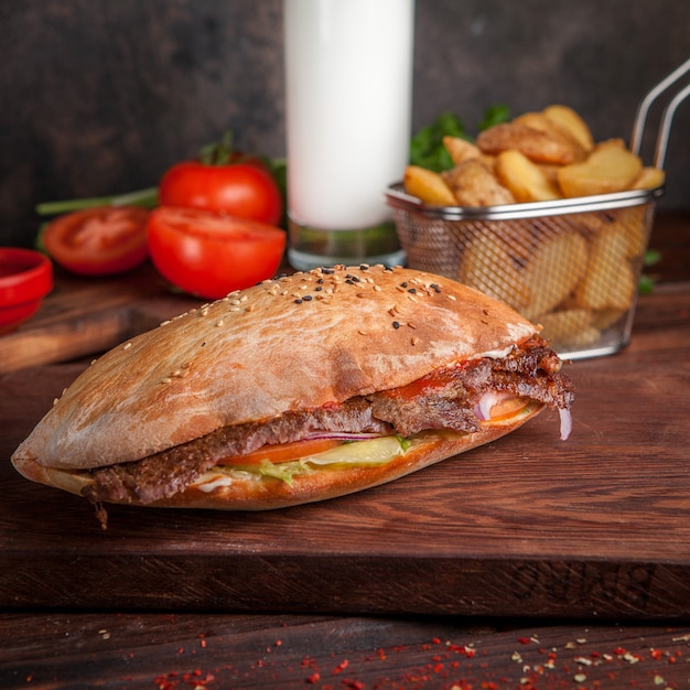 Side view doner with tomato and fried potatoes and ayran in board cookware