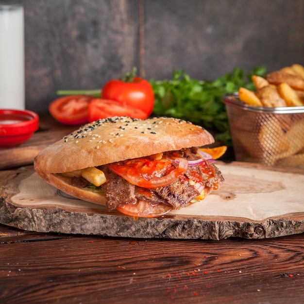 Side view doner with tomato and fried potatoes and greens in board cookware