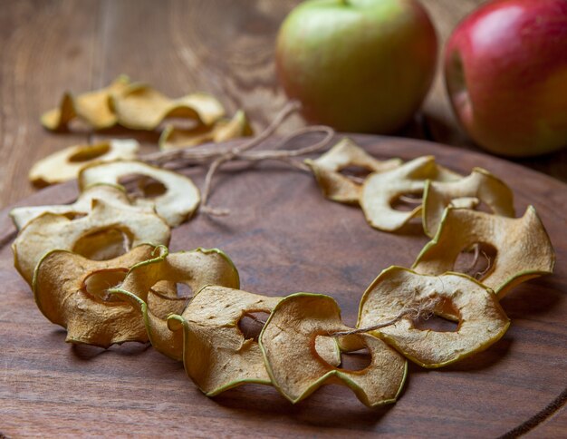 Side view dried apples on round cutting board and fresh apples on wooden table