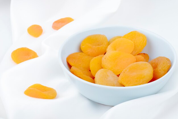 Side view of dried apricots in a white bowl on white background