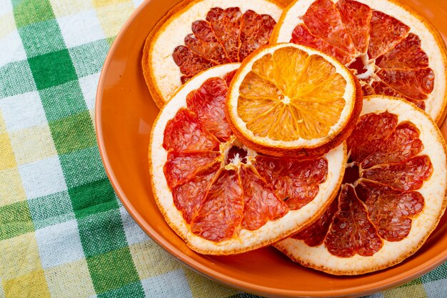 Side view of dried orange and grapefruit slices in a plate on plaid tablecloth