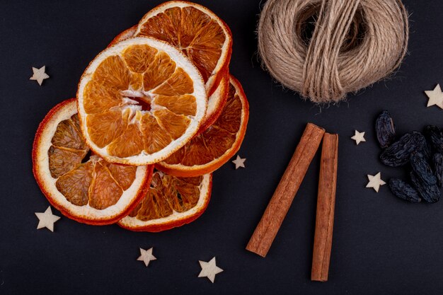 Side view of dried orange slices with cinnamon sticks arranged on black background