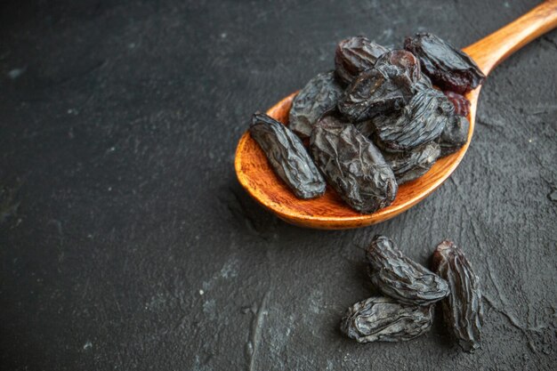 Side view of dry black cherry in a wooden spoon and on black background with free space