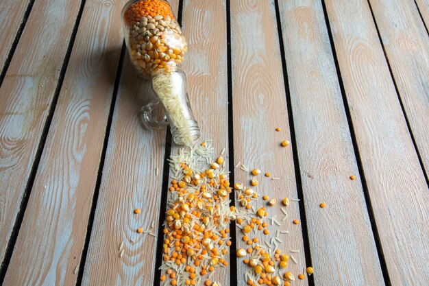 Side view of dry corn seeds and rice scattered from a glass bottle on rustic