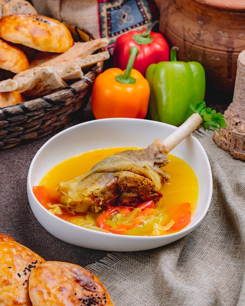 Side view of duck leg in bouillon with vegetables in a white bowl