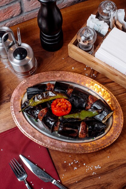 Side view of eggplant kebab with tomato and green pepper on a wooden table