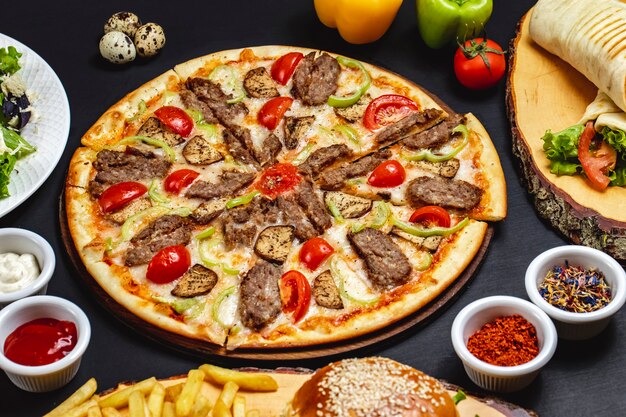 Вид сбоку пицца из баклажанов с жареными ломтиками красного мяса, помидор, баклажан, сыр и сладкий перец на столе