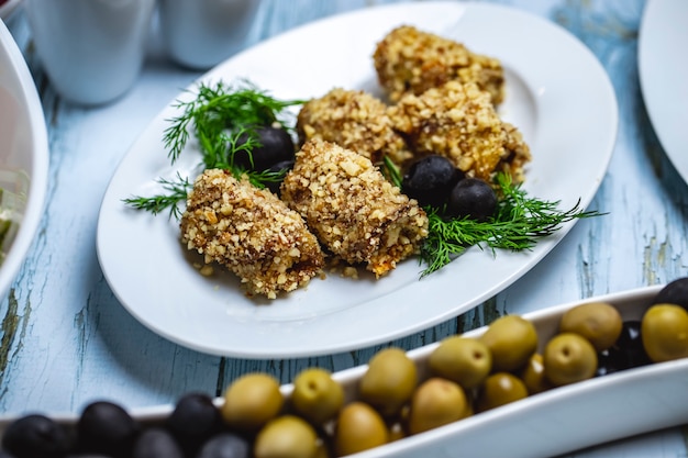 Free photo side view eggplant rolls with walnuts dill black and geen olives on the table