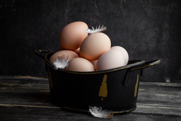 Free photo side view eggs in pot with feathers on dark wooden background. horizontal