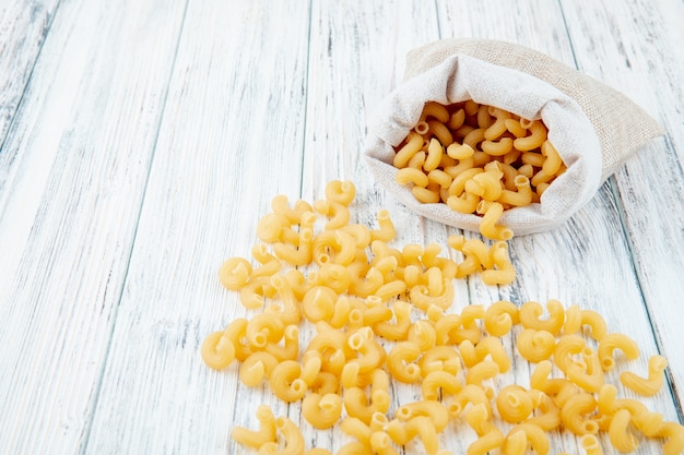 Foto gratuita pasta dei maccheroni del gomito di vista laterale in borsa su fondo di legno bianco