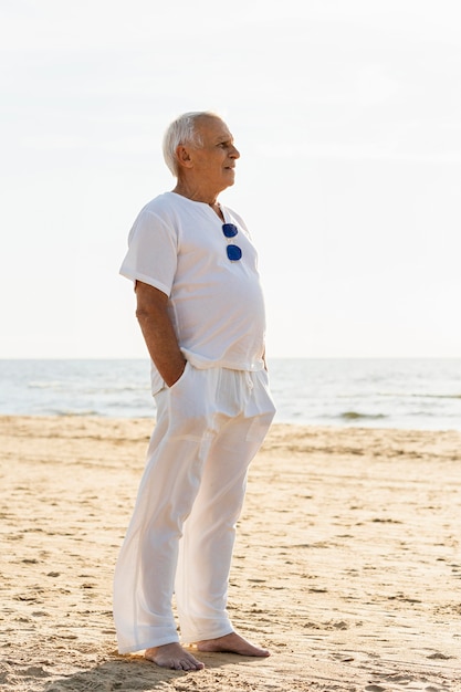 Вид сбоку пожилого мужчины в солнцезащитных очках, любуясь солнцем на пляже