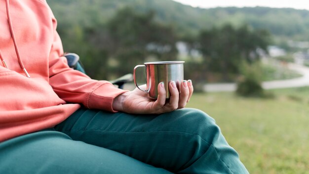 Side view of elder tourist woman holding metal cup outdoors