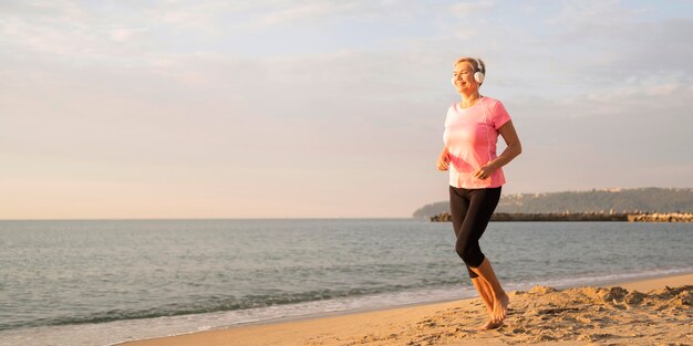 Side view of elder woman with headphones jogging on the beach