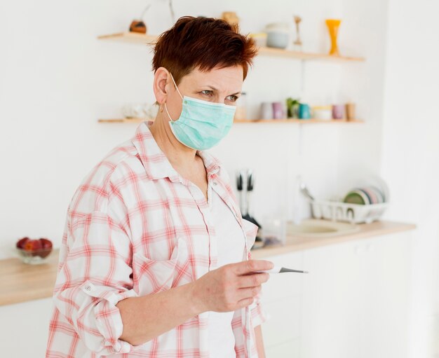 Side view of elder woman with medical mask holding thermometer