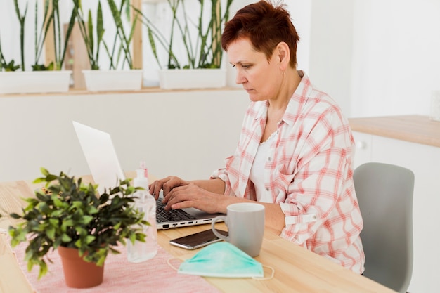 Вид сбоку старшей женщины, работающей на ноутбуке из дома