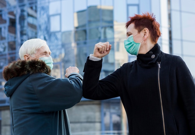 Free photo side view of elder women in the city touching elbows to salute each other