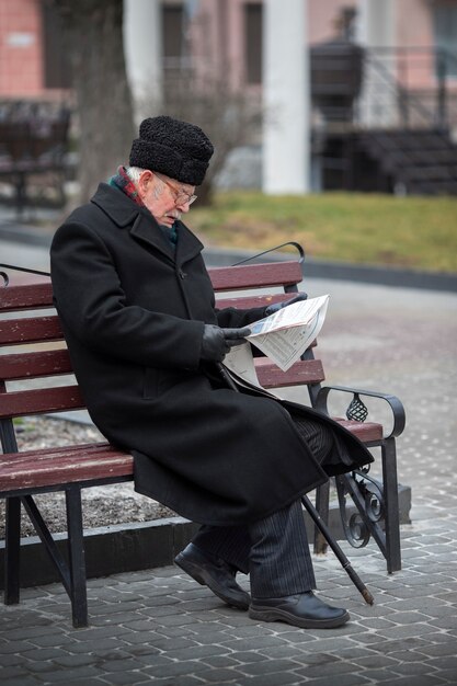 Side view elderly man reading newspaper