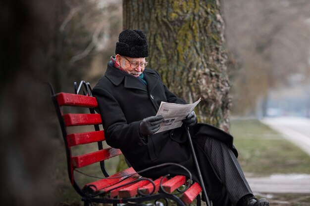 Side view elderly man reading newspaper
