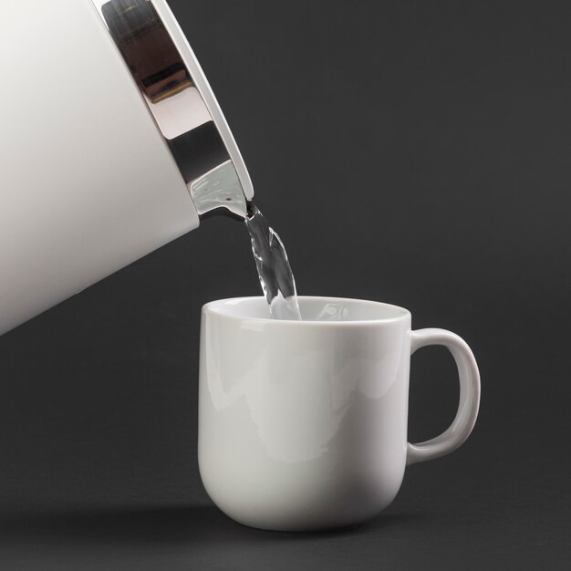 Side view electric kettle pouring water in cup