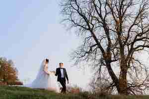 Free photo side view of elegant newlyweds walking holding hands in autumn park