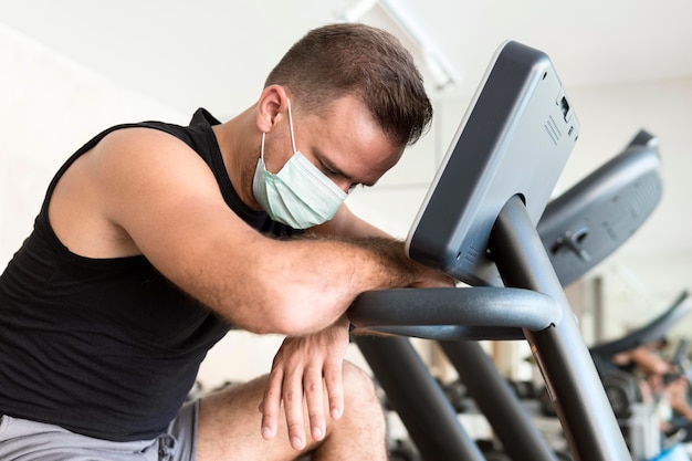 Side view of exhausted man with medical mask at the gym