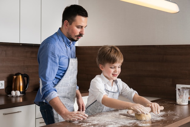 Free photo side view father and son rolling dough