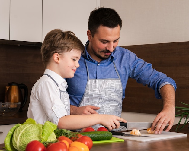 Side view father teaching son to cut vegetables
