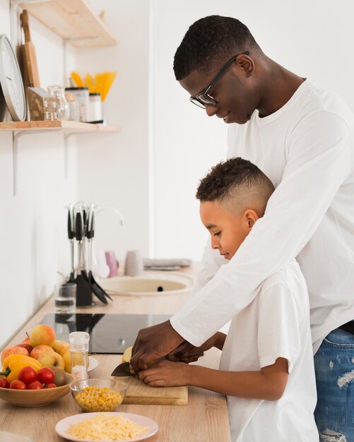 Side view father teaching son how to cut fruits