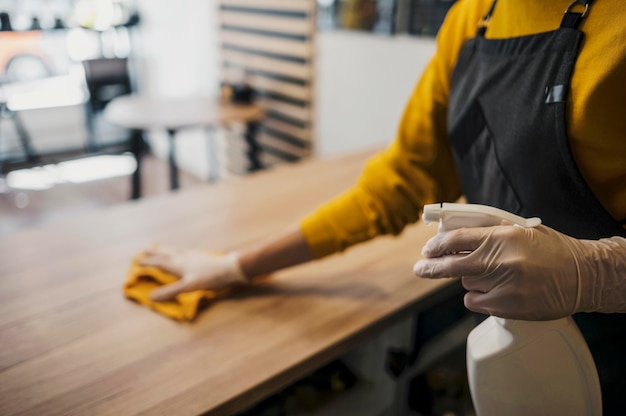 Side view of female barista cleaning table while wearing latex gloves