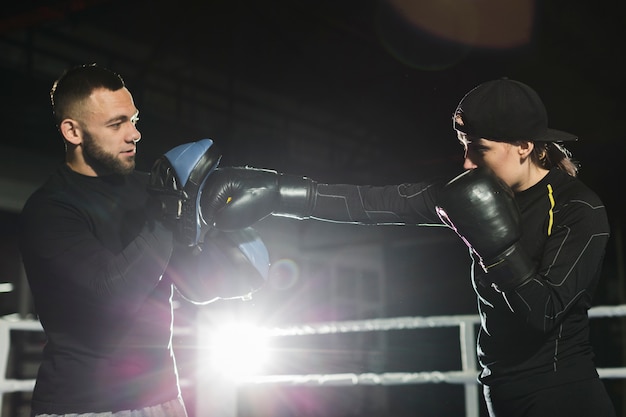 Side view of female boxer practicing in the ring with trainer