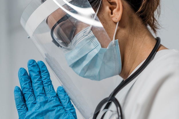 Side view of female doctor with face shield and medical mask praying