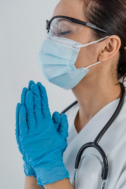 医療マスクと手袋を祈って女性医師の側面図