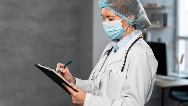 Side view of female doctor with medical mask and hairnet holding clipboard