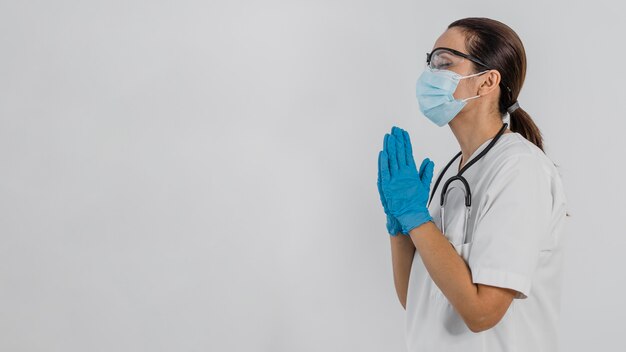 Вид сбоку на женщину-врача с медицинской маской, молящуюся с копией пространства