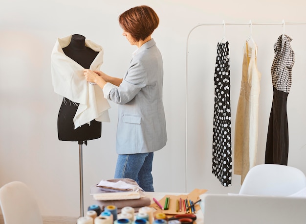 Free photo side view of female fashion designer in atelier with dress form