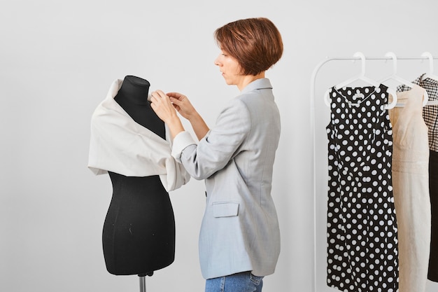 Free photo side view of female fashion designer working in atelier with dress form